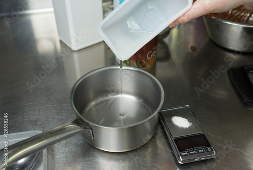 A container of clear sugar syrup being poured into a metal pan, ready for cooking.
