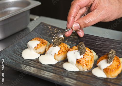 Delicious pan seared organic scallops, served with caviar, and white wine cream sauce. Presented professionally and shot with a shallow depth of field.