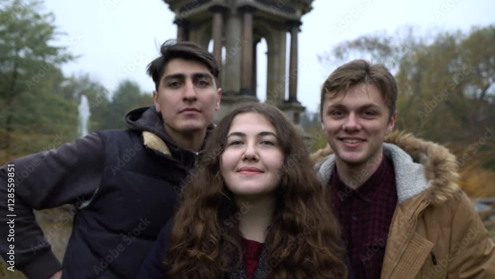 Threesome of friends taking photo together near a fountain and talking to eah other. Autumn landscape. Threesome of friends taking photo together near a fountain and talking to eah other. Autumn landscape.