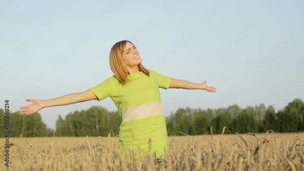 Happy girl in a green dress is waving her hands standing among ripe ears of wheat. Happy girl in a green dress is waving her hands standing among ripe ears of wheat.