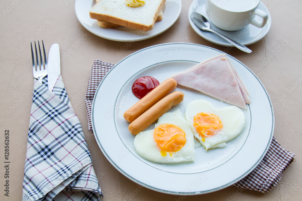 Breakfast with fried egg, ham, sausage, toast, butter, and coffee on table. Breakfast with fried egg, ham, sausage, toast, butter, and coffee on table.