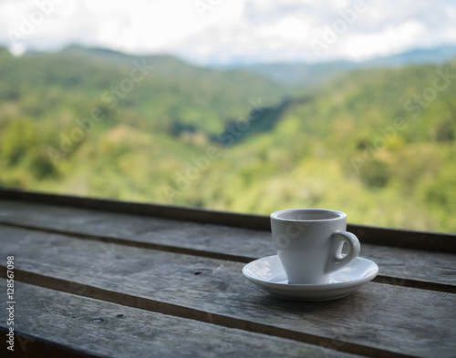 Cup of tea on wooden bar. Beauty nature background of mountains and tea plantation landscape at Doi-Montngo, Chiang Mai, Thailand