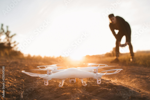 Pilot landing drone outdoor, sunset, free space. Close up of quadrocopter on ground, sun flare, copy space on sky. Entertainment, leisure, modern technologies concept