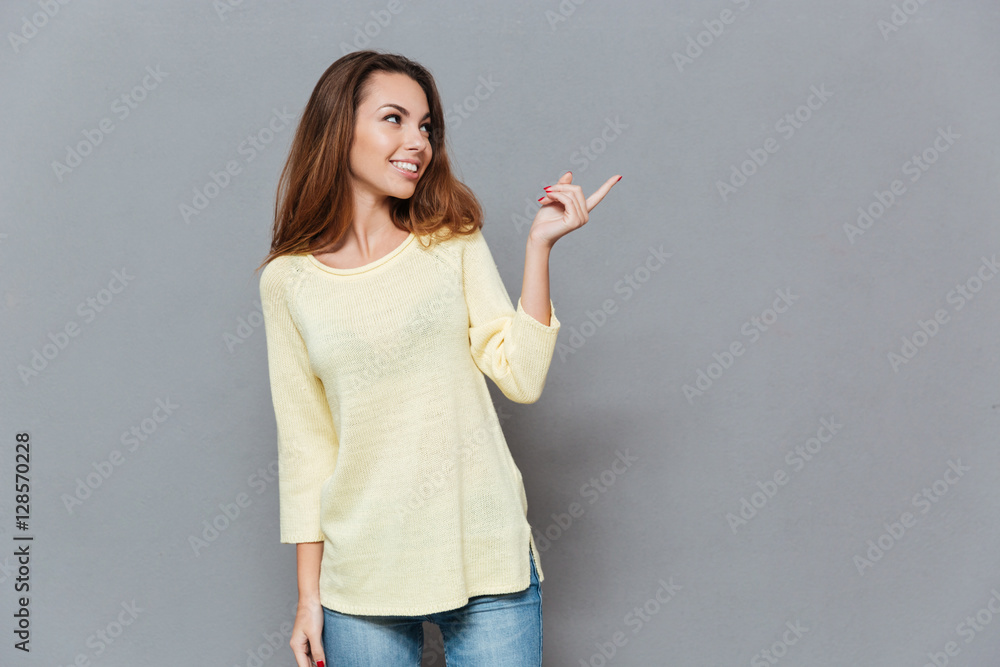Portrait of a smiling woman in sweater pointing finger away Portrait of a smiling woman in sweater pointing finger away