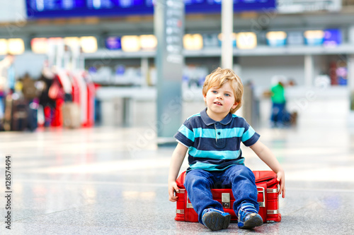 Little kid boy going on vacations trip with suitcase at airport