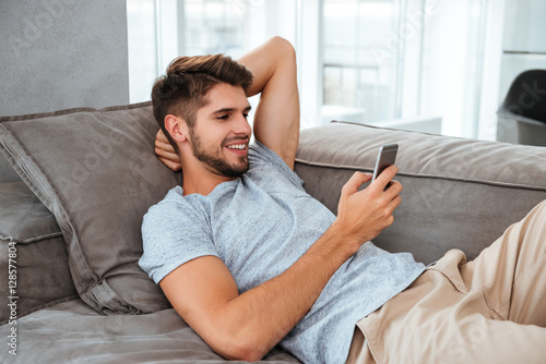Happy young man lies on sofa and chatting by phone