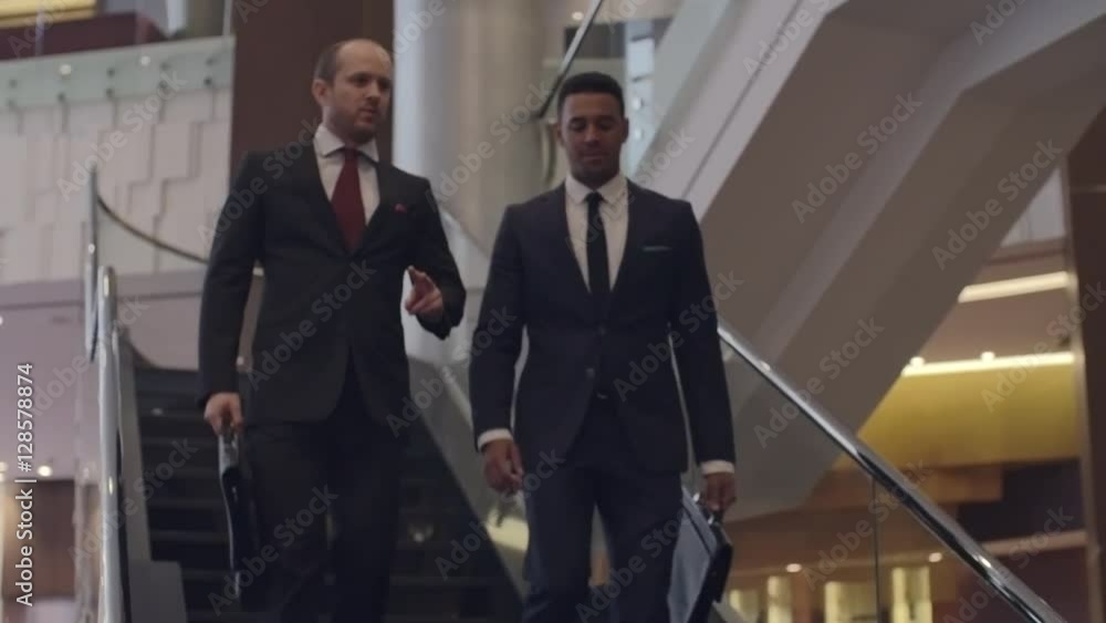 Two business partners talking and smiling while walking downstairs in the hotel Two business partners talking and smiling while walking downstairs in the hotel