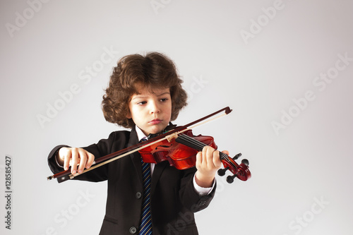 Little curly boy thoughtfully, playing a musical instrument. Gray background.