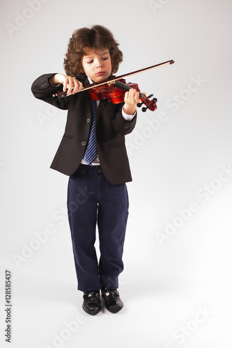 Funny little boy in a business suit playing the violin. Gray background.
