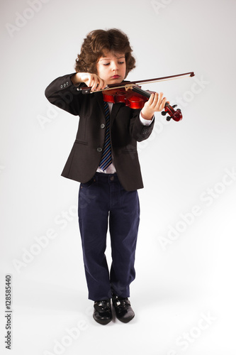 Clever little violinist in a business suit playing a musical instrument. Gray background.