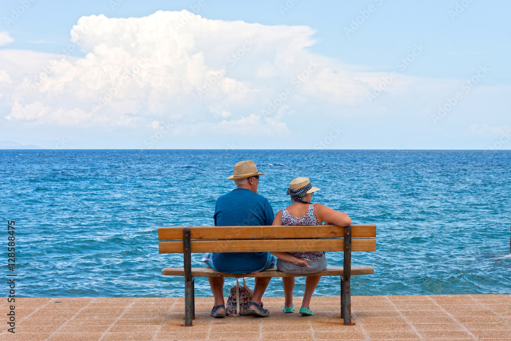 A copy of seniors sitting on a bench at sea shore