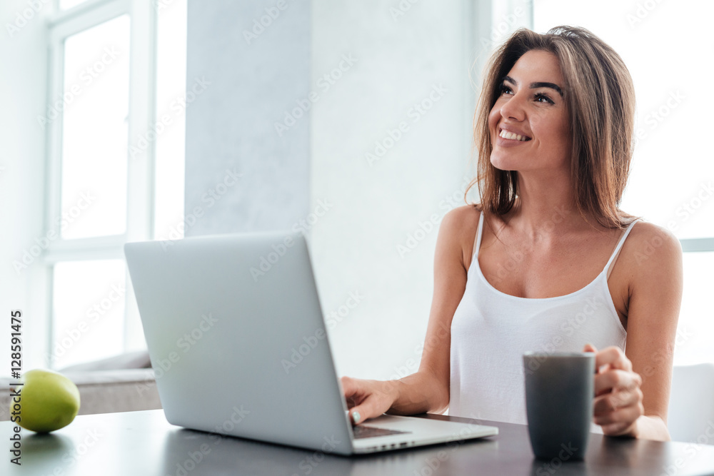 Happy woman using laptop and drinking coffee on the kitchen Happy woman using laptop and drinking coffee on the kitchen