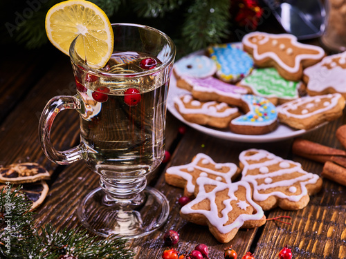 Christmas cookies on plate under fir branches. Christmas still life with mug decoration lemon slice hot drink on wooden table.
