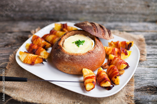 Tasty hot cheese fondue served in a bread roll with potatoes and photo