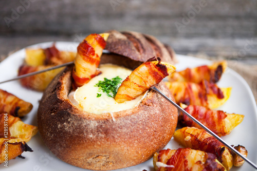 Tasty hot cheese fondue served in a bread roll with potatoes and