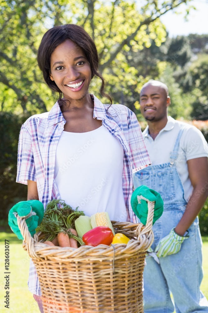Obraz premium Young woman holding a basket of freshly harvested vegetables