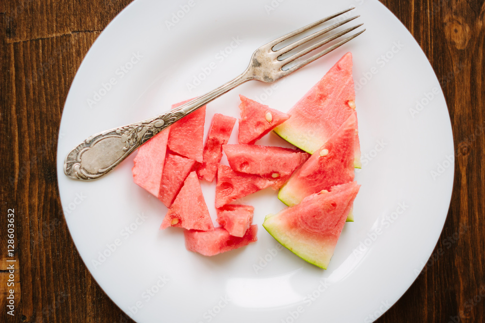 Small pieces of ripe watermelon and fork on the white plate over wooden background Small pieces of ripe watermelon and fork on the white plate over wooden background