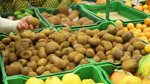 man picks fruit kiwi in the supermarket