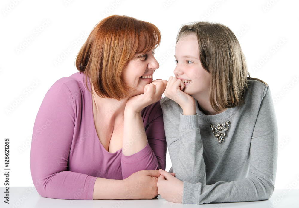 Woman and teen girl sitting together at a table and looking at e Woman and teen girl sitting together at a table and looking at e