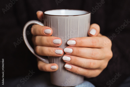 Woman with beautiful manicure holding a gray cup of tea