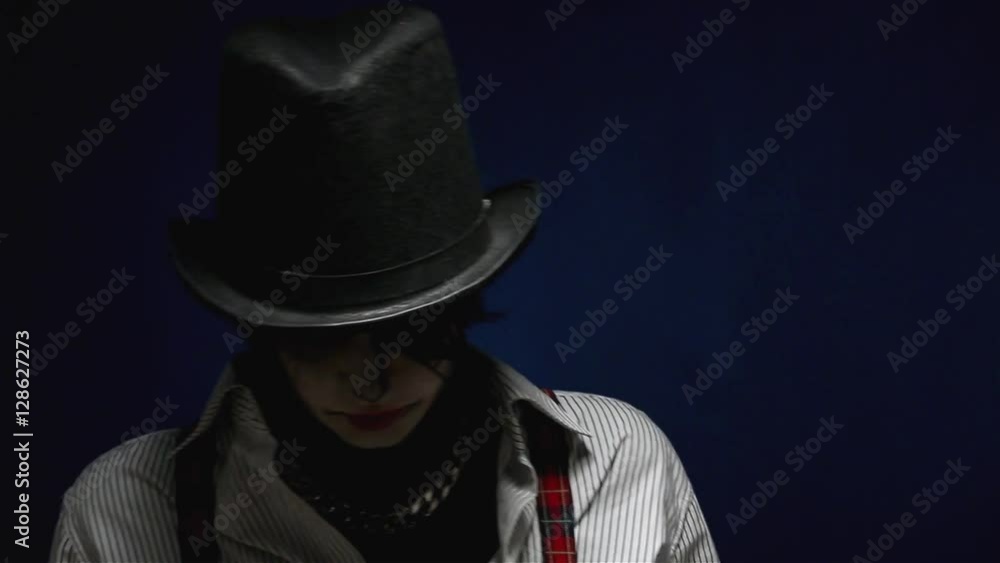 Portrait of frightened girl with Halloween makeup posing isolated on navy blue background. Lady with black hat on touching her face, smiling and looking frightened in studio. Woman showing tongue. Portrait of frightened girl with Halloween makeup posing isolated on navy blue background. Lady with black hat on touching her face, smiling and looking frightened in studio. Woman showing tongue.