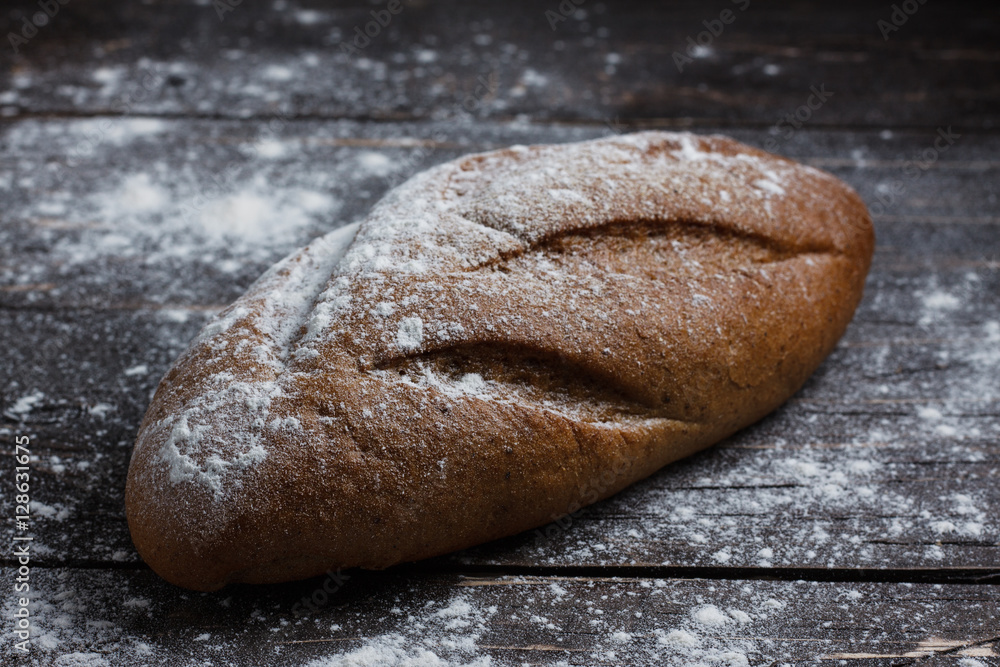 One black bread with flour on a wooden background. Advertising bread. Leaning flour. One black bread with flour on a wooden background. Advertising bread. Leaning flour.