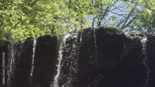 Slow motion shot of water coming over edge at waterfall in forest. photo