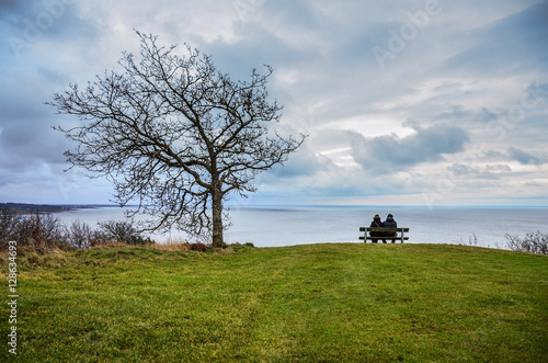 Two young people sitting on the bench over the sea and looking at the calm scenery