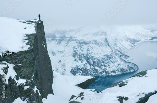 Konstfotografi Alone man standing over majestic landscape covered by snow with deep valley and big sharp mountains and huge lake