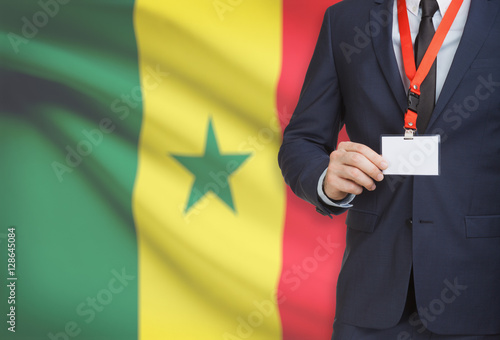 Businessman holding name card badge on a lanyard with a national flag on background - Senegal
