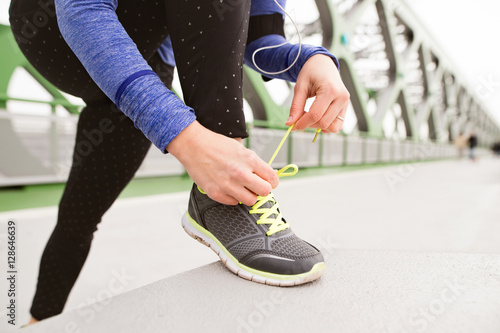 Unrecognizable runner in the city tying shoelaces on steel bridg