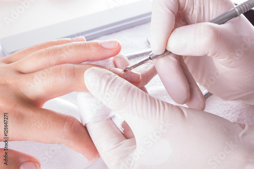 Nail technician giving customer a manicure at nail salon. Young caucasian woman receiving a french manicure. Closeup shot of a woman using a cuticle pusher to give a nail manicure.