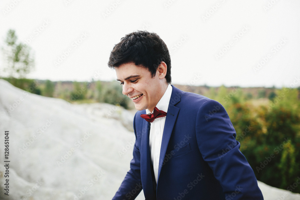 handsome and happy groom in a suit walking on sand quarry handsome and happy groom in a suit walking on sand quarry