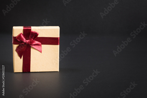 Paper gift box with deep red ribbon and a bow, on black background.