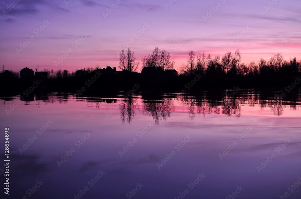 Beautiful colorful dusk on a river with silhouettes of houses and trees