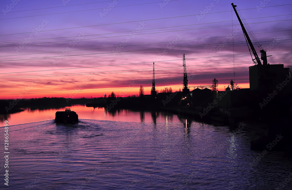 Beautiful colorful dusk on a river with silhouettes of barge and cranes