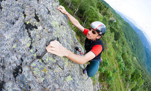 Young man climbing on a wall with green valley on the background