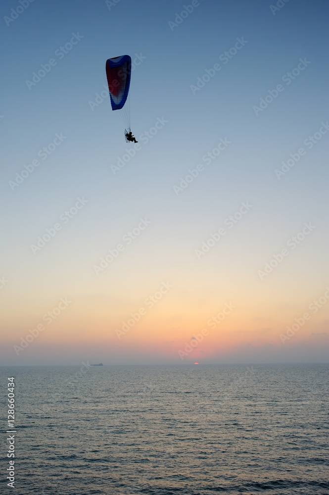 Powered paraglider flying over the sea at sunset sky background