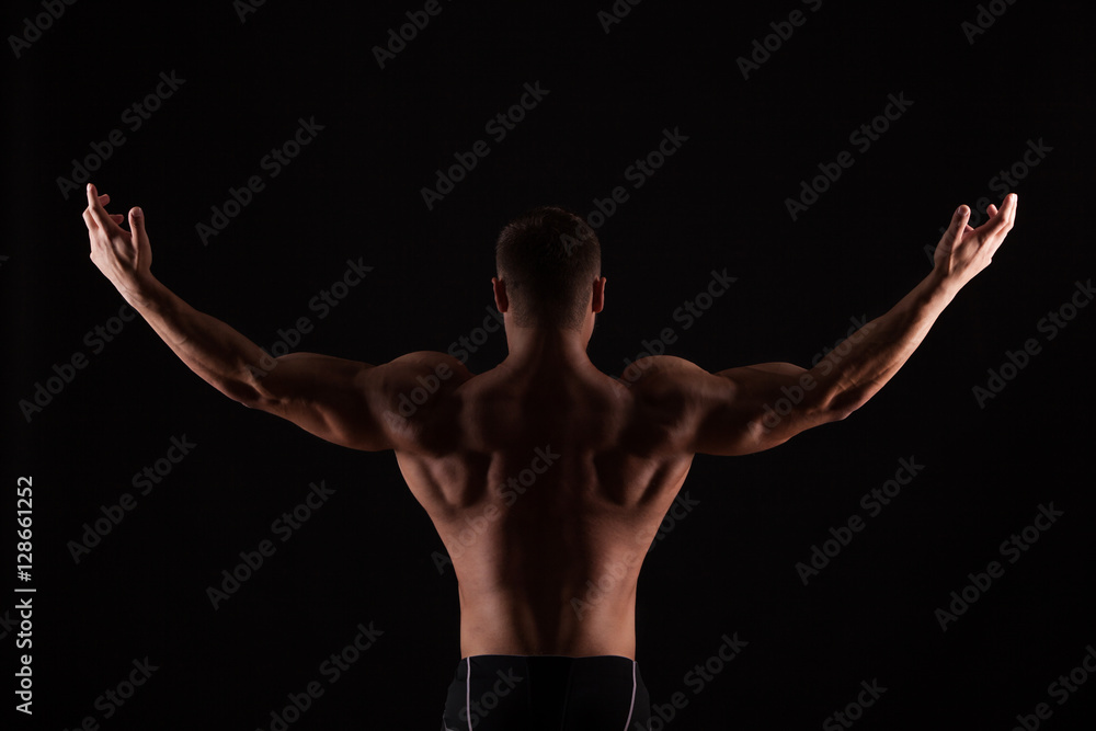 Rear view of healthy muscular young man with his arms stretched out isolated on black background