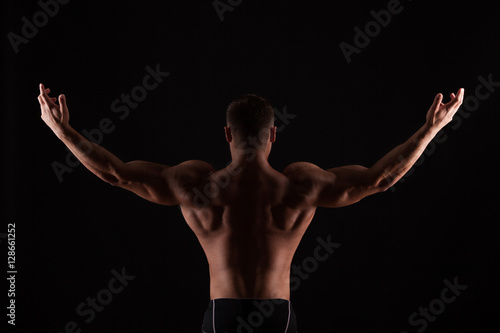 Rear view of healthy muscular young man with his arms stretched out isolated on black background