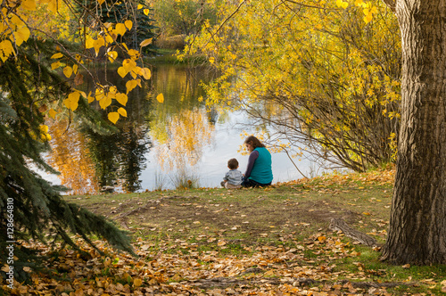 Mother and son sitting by a pond in a park