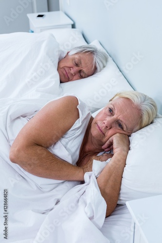 Thoughtful senior woman lying on bed 