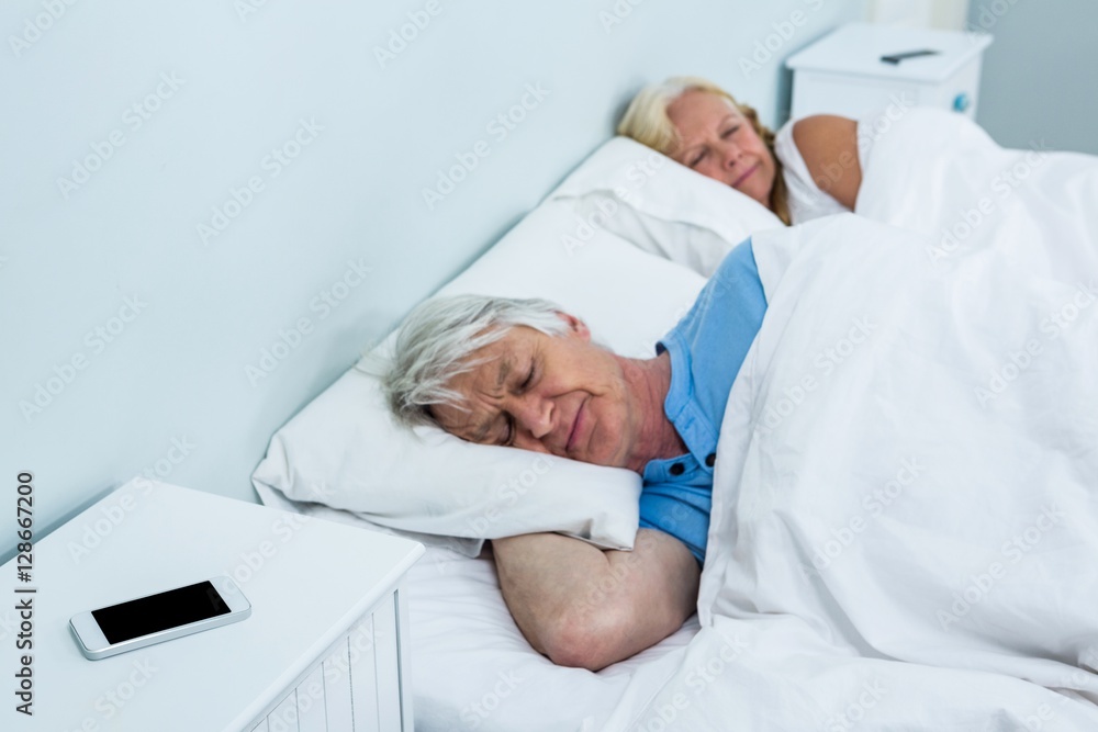 Senior couple resting on bed with phone on table Senior couple resting on bed with phone on table
