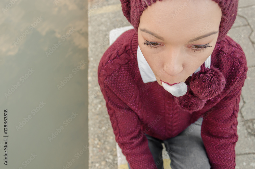 girl sits by the river and blows a bubble from bubble gum girl sits by the river and blows a bubble from bubble gum
