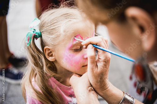 woman painting face of kid outdoors