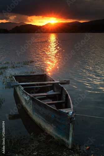 Colorful summer sunset over lake with an old rowing boat in the foreground. © rogit