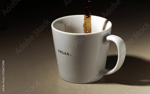 Super slow motion pouring of coffee into a coffee mug, with drops of coffee and coffee splashing, spilling.