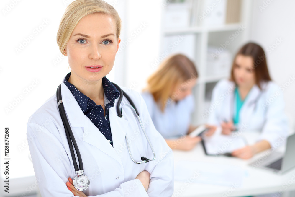 Female doctor smiling on the background with patient and his physician in hospital Female doctor smiling on the background with patient and his physician in hospital