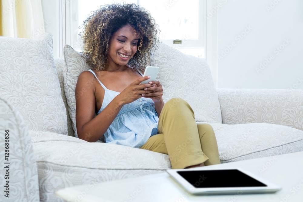 Young woman sitting on sofa and text messaging on phone Young woman sitting on sofa and text messaging on phone