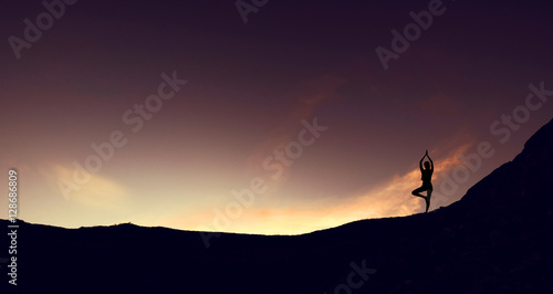 Silhouette mountain edge young woman practicing yoga on mountain in sunrise © SasinParaksa